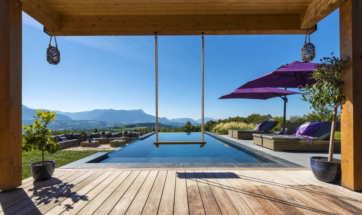 Piscine à débordement vue depuis une terrasse en bois couverte, face aux montagnes