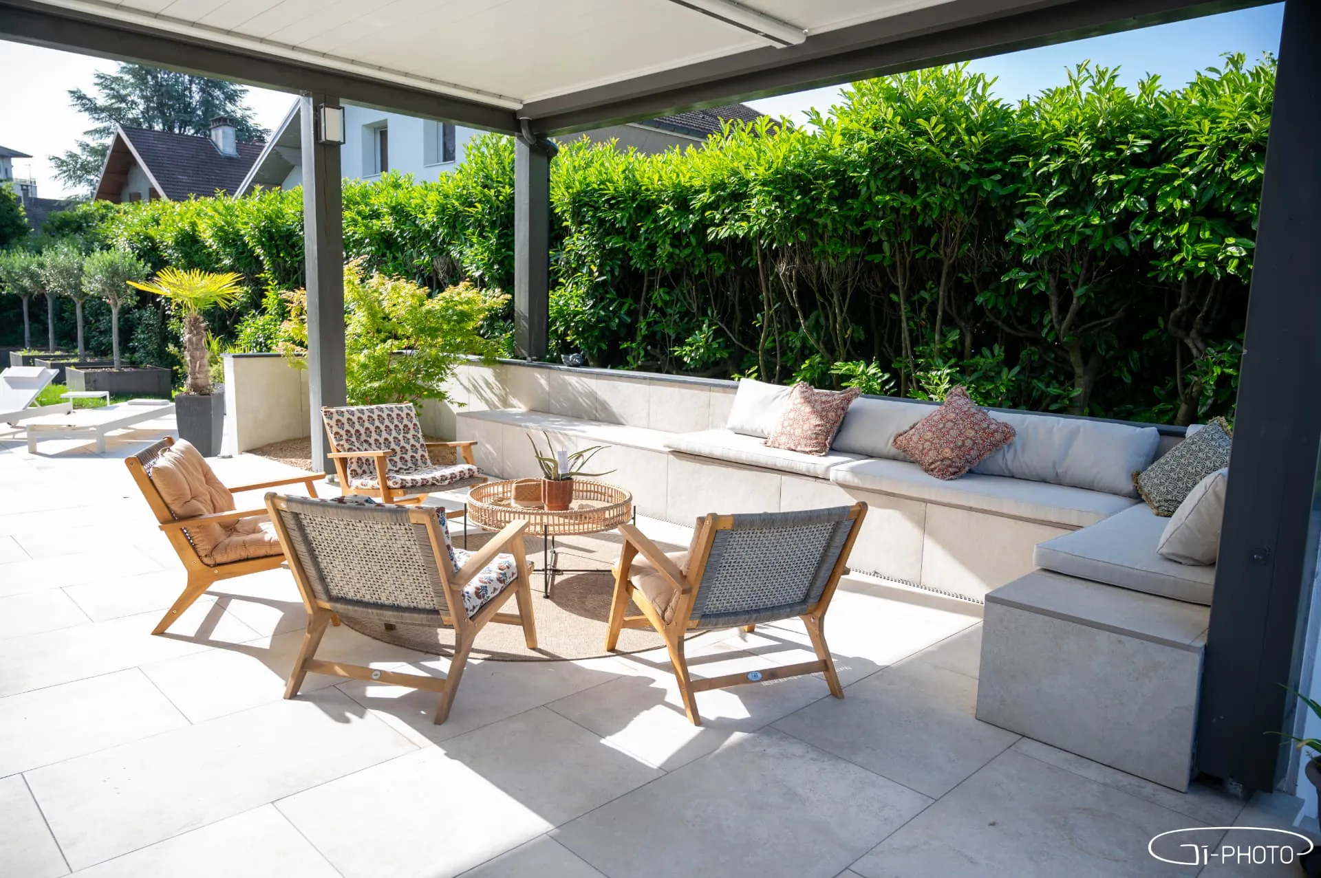 Salon extérieur sous pergola avec banquette maçonnée et haie végétale – Rumilly