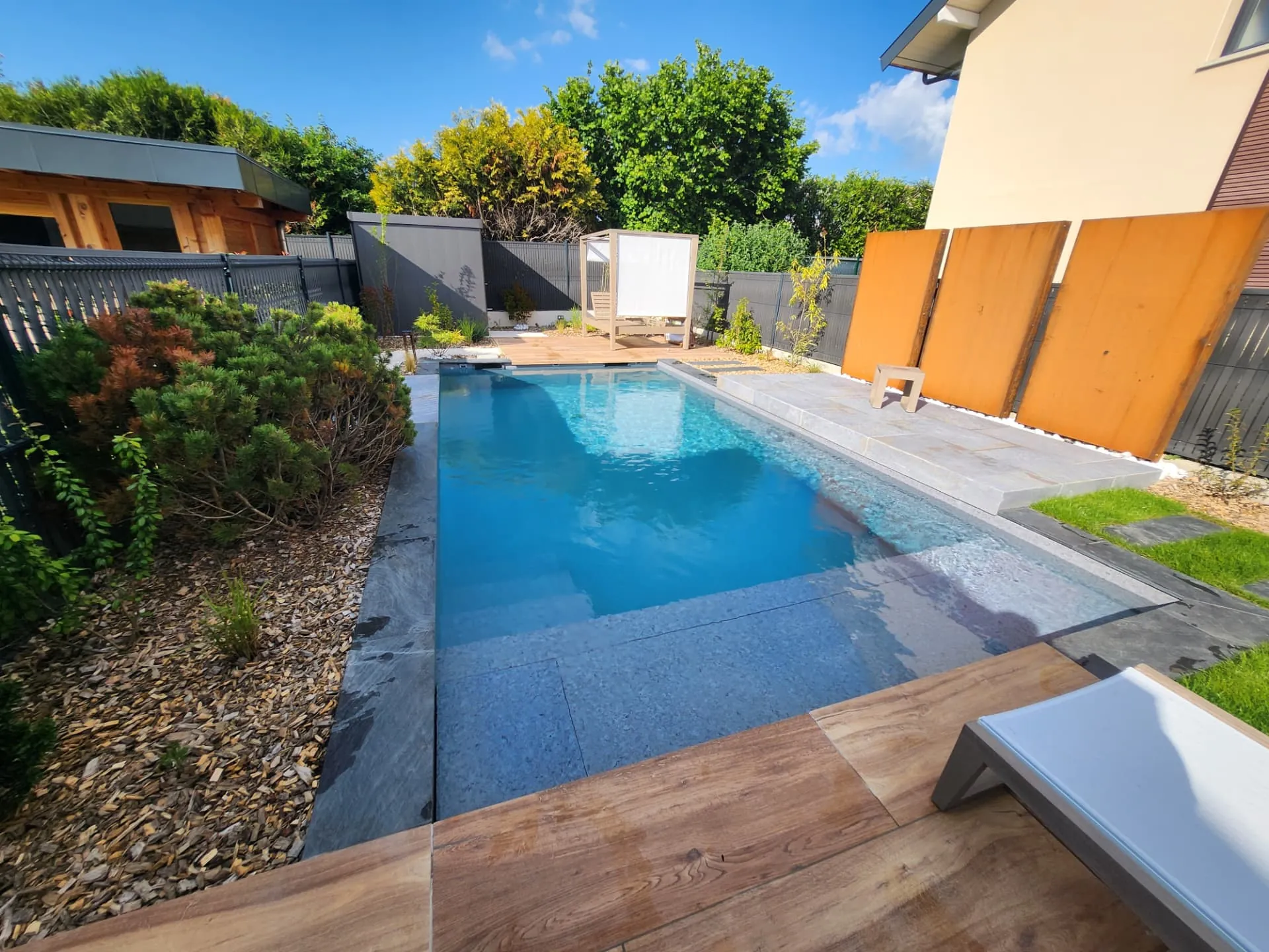 Jardin contemporain : piscine, dallage, terrasse effet bois et panneaux en acier corten