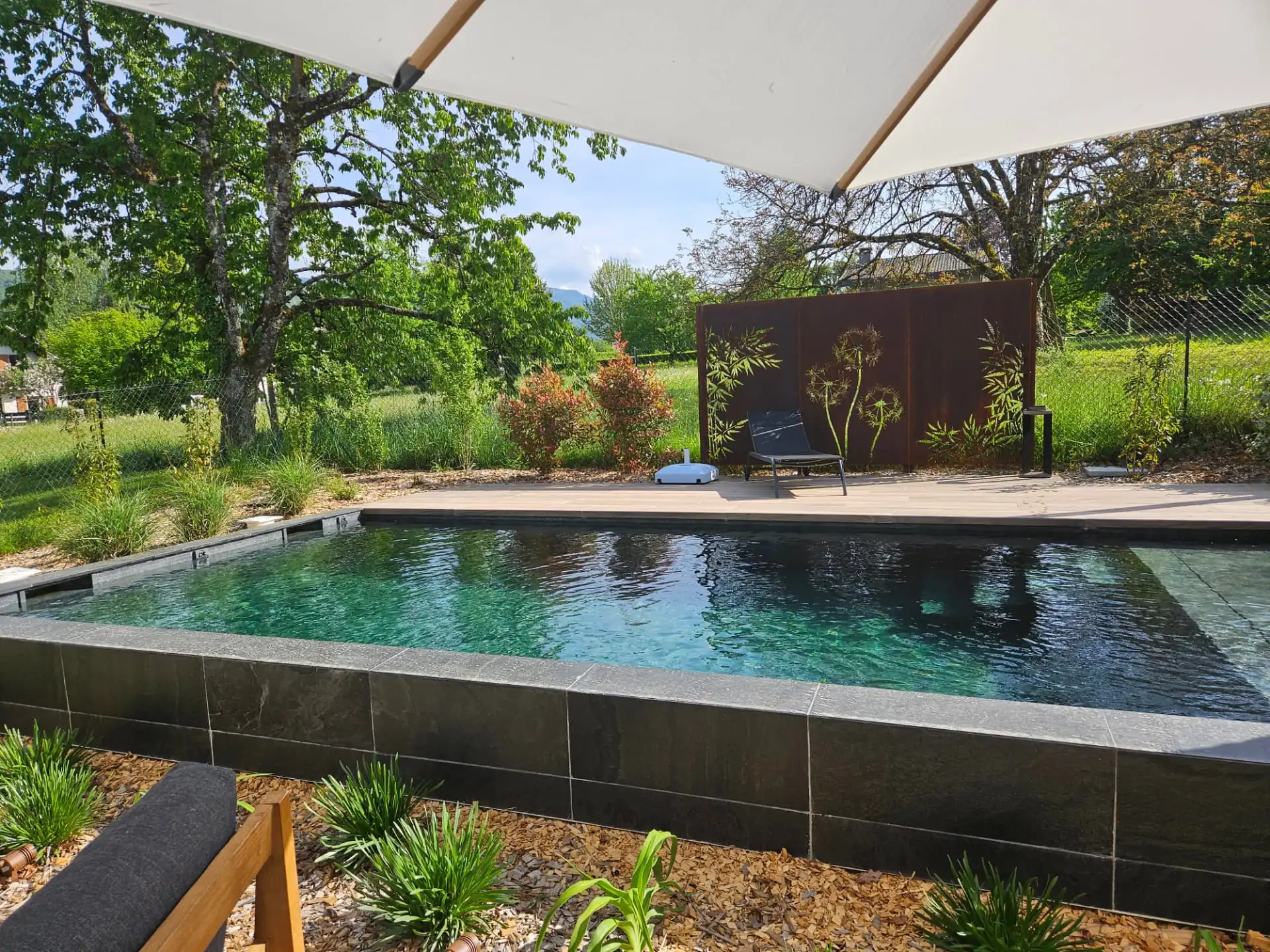Piscine bordée de pierre sombre et de plantations, panneau en acier corten – Seynod