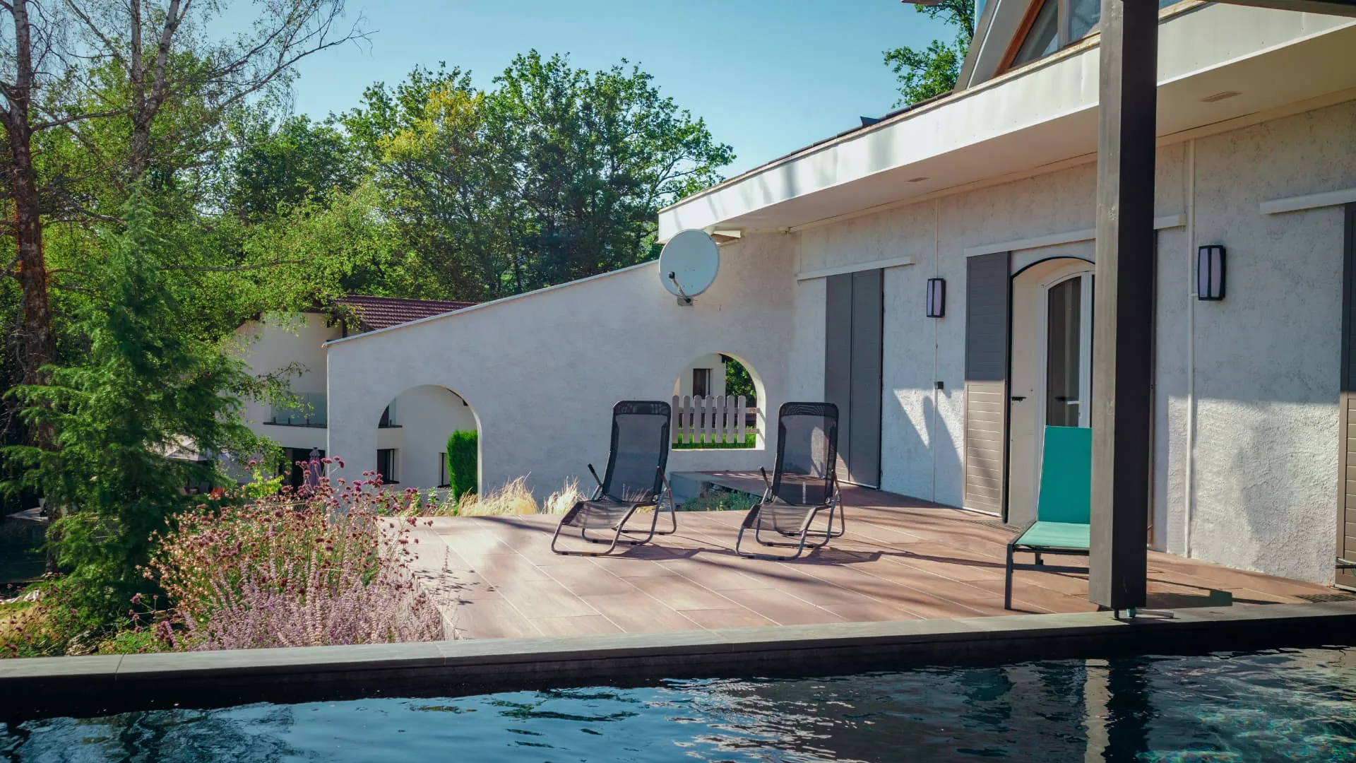 Terrasse en bois avec transats au bord de la piscine, massifs fleuris – Pringy