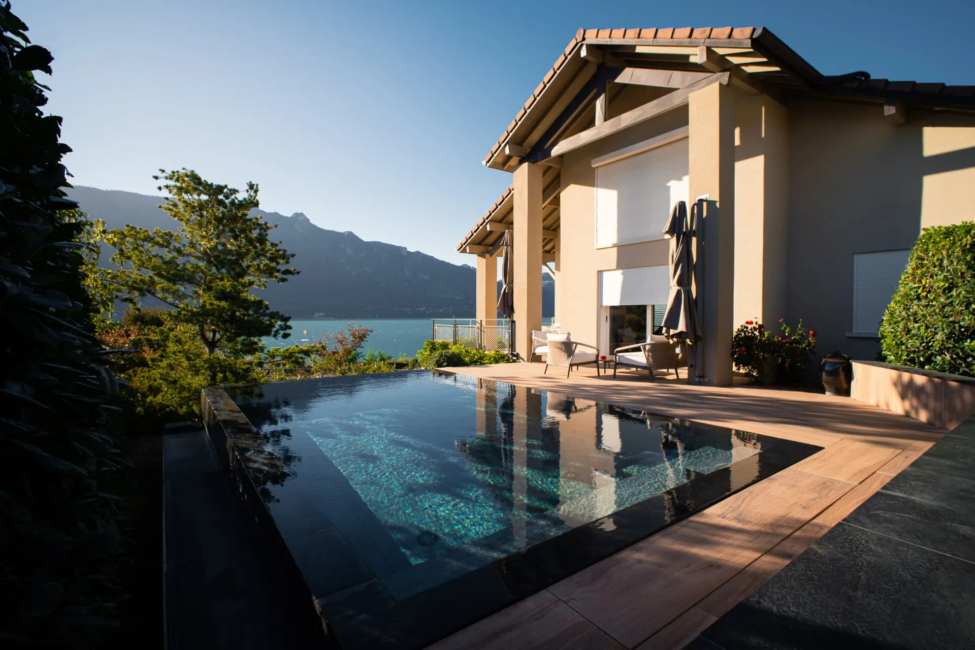 Piscine à débordement en pierre sombre devant la maison, lac en arrière-plan – Viviers-du-Lac
