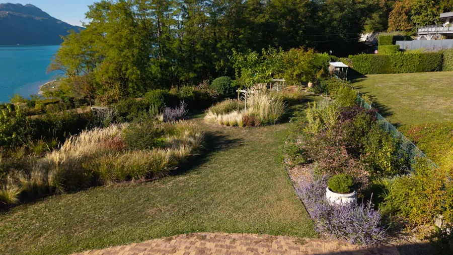 Jardin en pente avec pelouse, graminées et massifs fleuris face au lac – Viviers-du-Lac